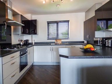 A kitchen with black countertops white cabinets a window with blinds and kitchen appliances at Tehidy in Charlestown