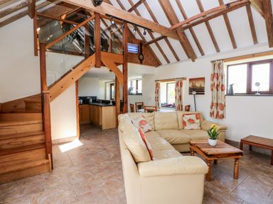 A living room with a beige sectional sofa and wooden coffee table next to a staircase and kitchen at The Long Barn in Hasguard near Little Haven