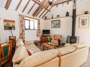 A living room with a cream sectional sofa a wooden coffee table an armchair wood stove and TV at The Long Barn in Hasguard near Little Haven