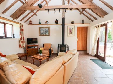 A living room with beige sofas a wooden coffee table a wood stove a TV on a wooden stand and exposed wooden beams at The Long Barn in Hasguard near Little Haven