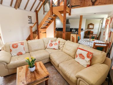 A living room with a beige sectional sofa with orange floral pillows and a wooden coffee table with a yellow flower pot at The Long Barn in Hasguard near Little Haven