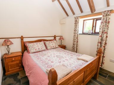 A bedroom with a wooden bed with patterned bedding and two bedside tables with lamps at The Long Barn in Hasguard near Little Haven