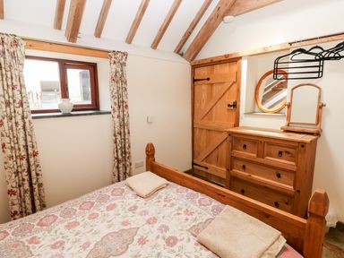 A bedroom with a wooden bed and dresser with a mirror near a window and wooden door at The Long Barn in Hasguard near Little Haven