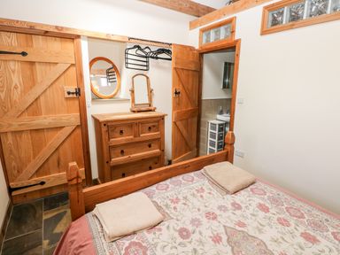 A bedroom with a wooden bed, floral bedspread, dresser with mirror, hanging hangers, and wooden doors at The Long Barn in Hasguard near Little Haven