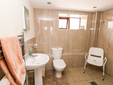 A bathroom with a sink toilet towel rail and chair at The Long Barn in Hasguard near Little Haven