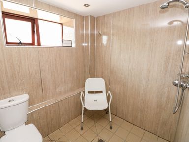 A bathroom with a toilet shower head and a white plastic chair at The Long Barn in Hasguard near Little Haven