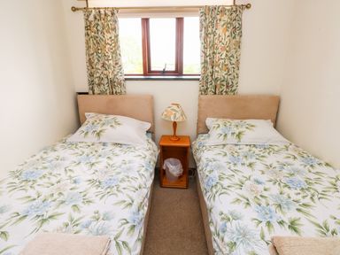 A bedroom with two single beds floral bedding wooden nightstand and lamp at The Long Barn in Hasguard near Little Haven