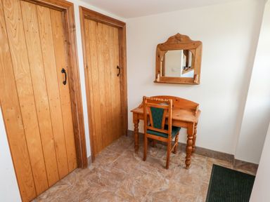 A corner with two wooden doors a wooden desk with a green upholstered chair and a wooden framed mirror on the wall at The Long Barn in Hasguard near Little Haven