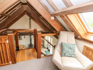 An attic space with wooden beams a leather chair with a cushion and a window at The Long Barn in Hasguard near Little Haven