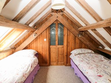 An attic bedroom with wooden beams two single beds and a wooden door at The Long Barn in Hasguard near Little Haven