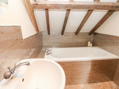 A bathroom with a bathtub under wooden ceiling beams and a sink with a faucet at The Long Barn in Hasguard near Little Haven