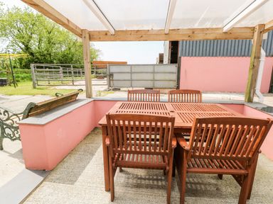 An outdoor seating area with a wooden table and four chairs under a clear roof at The Long Barn in Hasguard near Little Haven