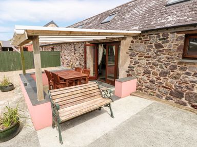 An outdoor patio with a wooden bench a wooden table with chairs and a covered seating area at The Long Barn in Hasguard near Little Haven