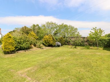 A fenced garden with a grass lawn and various shrubs and trees at The Long Barn in Hasguard near Little Haven