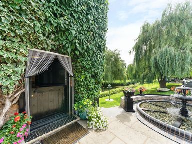 A black door with chain curtains surrounded by ivy next to a stone patio with a round water fountain and green lawn with trees and flowers at Grafton Mill in Grafton Flyford near Pershore