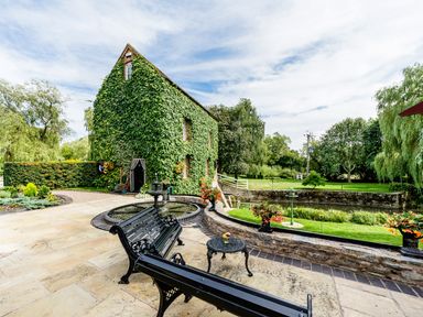 An ivy-covered building next to a fountain and benches with a garden and trees in the background at Grafton Mill in Grafton Flyford near Pershore