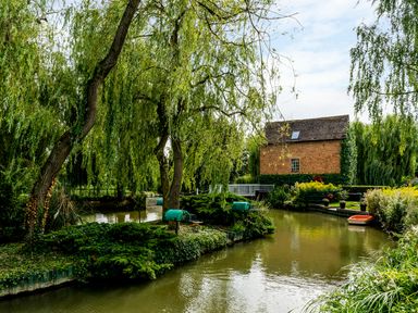 A canal with overhanging trees next to a brick house with a small boat on the water at Grafton Mill in Grafton Flyford near Pershore