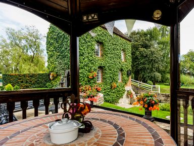 A round tiled table with a white dish and flowers under a wooden gazebo with an ivy-covered building and garden outside at Grafton Mill in Grafton Flyford near Pershore