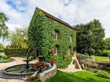 An ivy-covered building next to a circular water fountain and a stone walkway at Grafton Mill in Grafton Flyford near Pershore