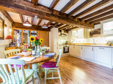 A kitchen with wooden beams on the ceiling a dining table with chairs sunflowers and fruit bowl at Grafton Mill in Grafton Flyford near Pershore