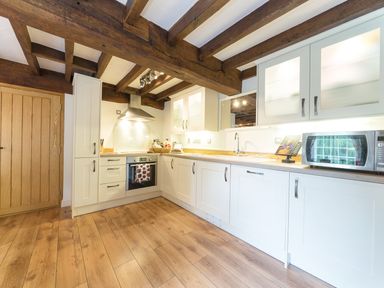 A kitchen with white cabinets wooden beams on the ceiling and wooden floor at Grafton Mill in Grafton Flyford near Pershore