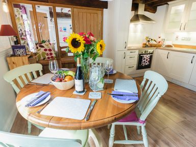 A kitchen and dining area with a wooden round table set with plates glasses and cutlery and a vase of sunflowers and fruit bowl at Grafton Mill in Grafton Flyford near Pershore