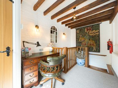 A small office area with a wooden desk and green leather chair near a staircase with wooden railing and a tapestry on the wall at Grafton Mill in Grafton Flyford near Pershore