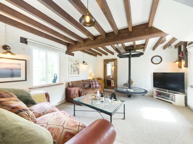 A living room with wooden beams on the ceiling a glass coffee table leather sofas a wall mirror a television and a round hanging shelf at Grafton Mill in Grafton Flyford near Pershore