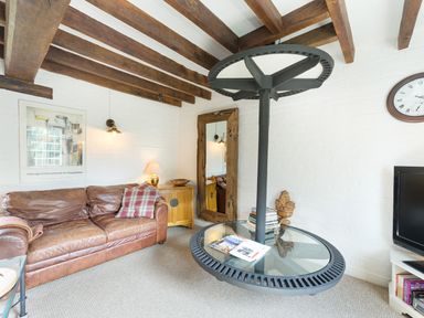 A living room with a brown leather sofa a wooden side table a large mirror a round glass coffee table and a wall clock at Grafton Mill in Grafton Flyford near Pershore