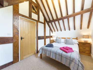 A bedroom with a wooden bed with pillows and folded towels on a blanket two wooden bedside tables with lamps and exposed wooden beams on the ceiling at Grafton Mill in Grafton Flyford near Pershore