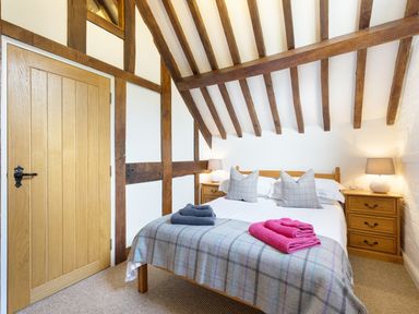 A bedroom with a wooden bed two bedside tables lamps and folded towels on the bed at Grafton Mill in Grafton Flyford near Pershore