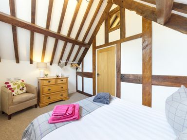 A bedroom with a bed pillow and folded towels a wooden chest of drawers armchair and wooden door at Grafton Mill in Grafton Flyford near Pershore