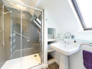 A bathroom with a shower, sink, shelves with baskets, and a window at Grafton Mill in Grafton Flyford near Pershore