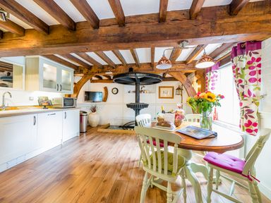 A kitchen and dining area with wooden beams a wooden table with chairs flowers on the table and white cabinets at Grafton Mill in Grafton Flyford near Pershore