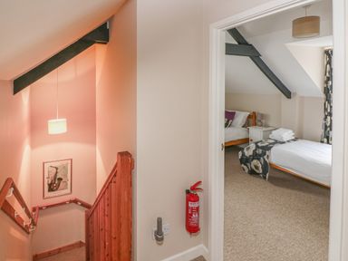 A stairway with wooden railing and a bedroom with two beds and a nightstand at Kingfisher in Blaenwaun