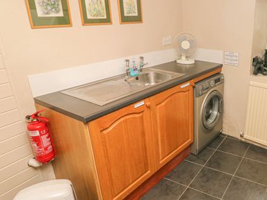 A utility room with a sink washing machine red fire extinguisher and fan at Kingfisher in Blaenwaun