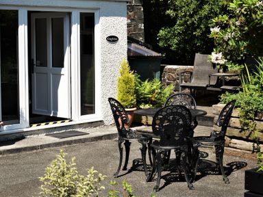 An outdoor patio with a black metal table and four chairs near a white door at Kingfisher in Blaenwaun