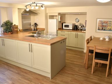 A kitchen with wooden countertops a dining table with chairs a microwave and a plant at Kingfisher in Blaenwaun