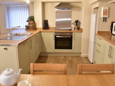 A kitchen with oven sink refrigerator wooden table and chairs at Kingfisher in Blaenwaun
