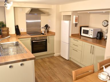 A kitchen with an oven sink refrigerator microwave kettle and wooden chairs at Kingfisher in Blaenwaun