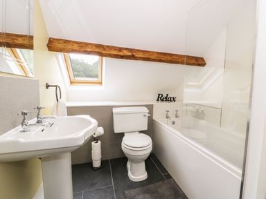 A bathroom with a sink toilet bathtub skylight windows and wooden beam at Hen Gelligemlyn - The Annexe in Ganllwyd