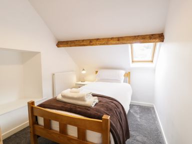 A small bedroom with a single bed with white linens and brown blanket under a wooden ceiling beam at Hen Gelligemlyn - The Annexe in Ganllwyd