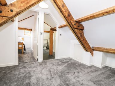 A carpeted attic room with exposed wooden beams and doors leading to a bedroom and a bathroom at Hen Gelligemlyn - The Annexe in Ganllwyd