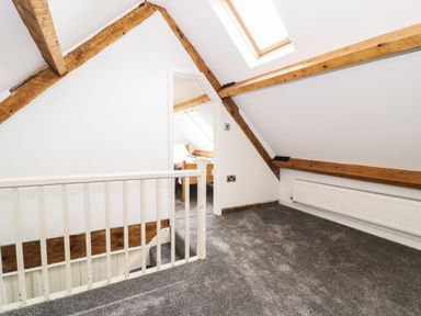 A carpeted loft area with wooden beams a white railing and a doorway leading to another room at Hen Gelligemlyn - The Annexe in Ganllwyd