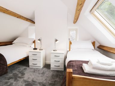 A bedroom with two single beds and bedside tables with lamps under a sloped ceiling at Hen Gelligemlyn - The Annexe in Ganllwyd