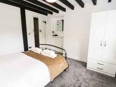 A bedroom with a bed covered in white and brown linens two stacks of towels a white wardrobe a small shelf with a mirror and a hairdryer at Hen Gelligemlyn - The Annexe in Ganllwyd