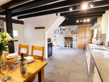A kitchen and dining area with a wooden table set for two a stone fireplace and wooden cabinets at Hen Gelligemlyn - The Annexe in Ganllwyd