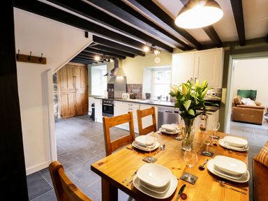 A kitchen and dining area with wooden table set for six and flowers on the table at Hen Gelligemlyn - The Annexe in Ganllwyd