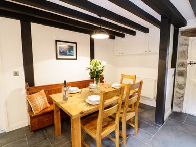 A dining area with a wooden table and chairs a bench with a cushion flowers on the table and a framed picture on the wall at Hen Gelligemlyn - The Annexe in Ganllwyd
