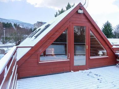 A snow-covered deck with a red triangular cabin with glass doors and windows at Strathavon Chalet in Aviemore